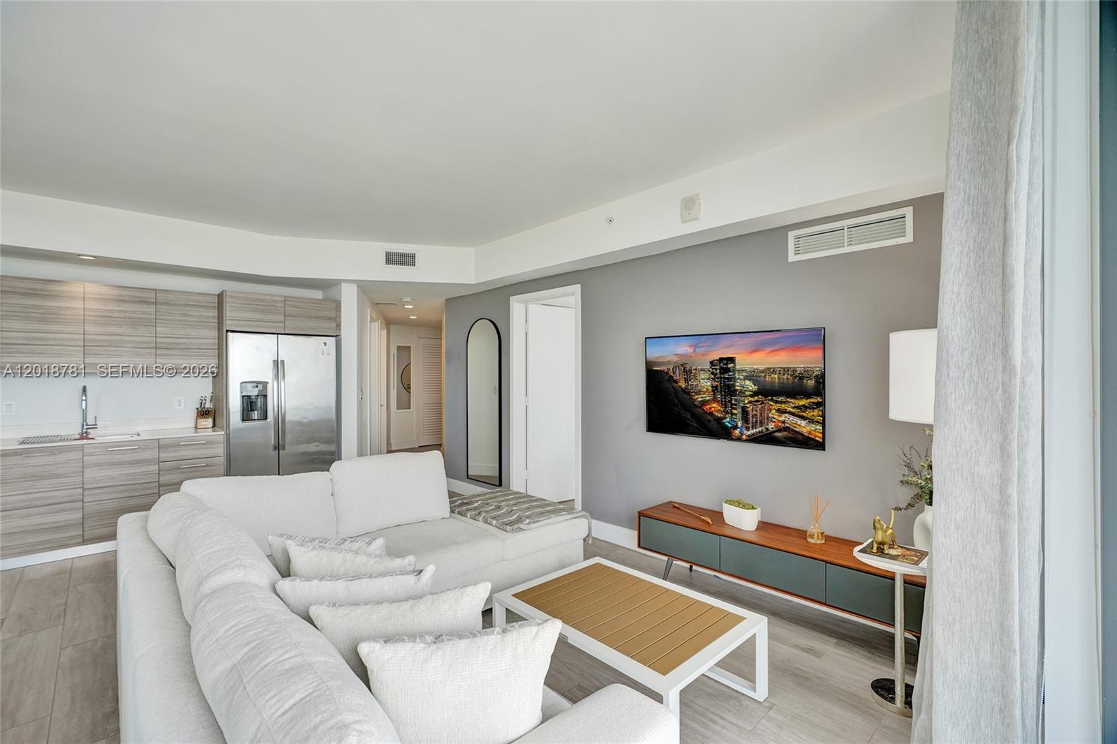 A living room features a white sectional sofa, a wall-mounted television, and an adjacent kitchen — 121 NE 34th St # 2809, Miami FL 33137, MIAMI, FL