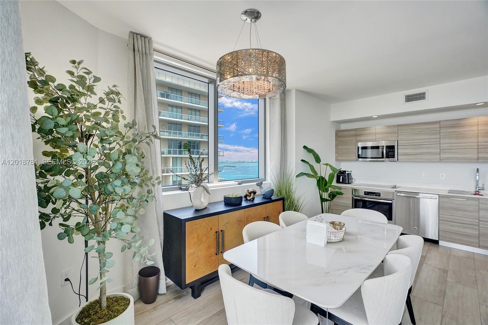 A modern dining area features a marble table, a wooden sideboard, and a waterfront view — 121 NE 34th St # 2809, Miami FL 33137, MIAMI, FL