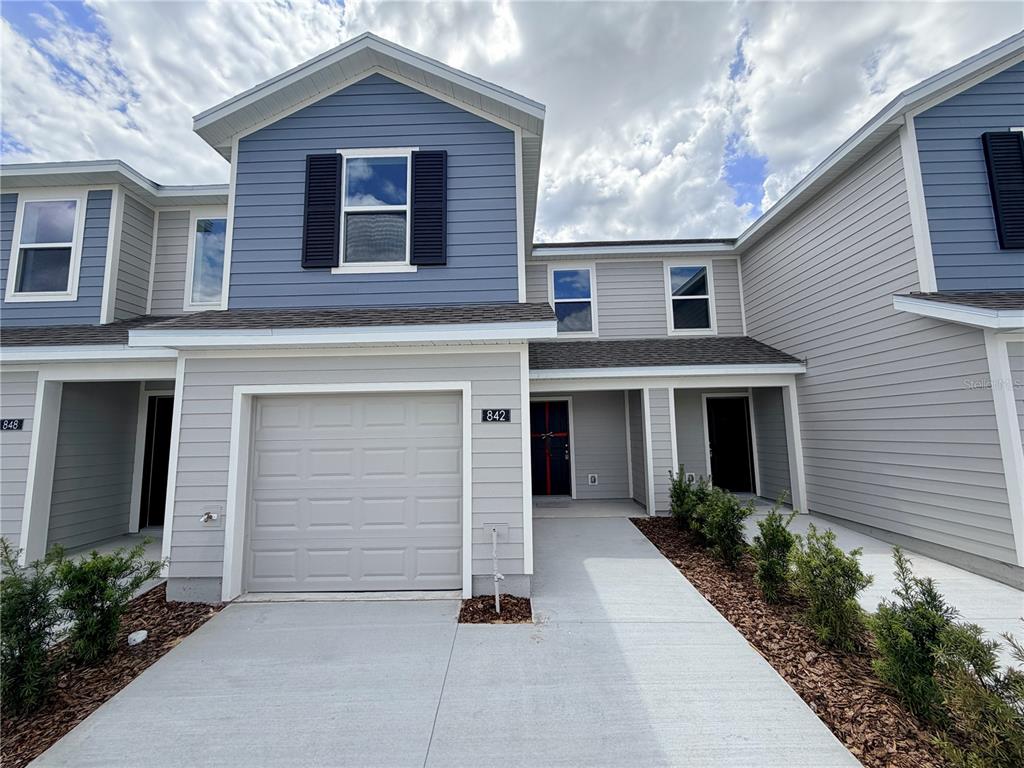 A two-story townhouse exterior features light gray horizontal siding, a blue gable, and a garage — 842 LYNX STREET, DAVENPORT, FL
