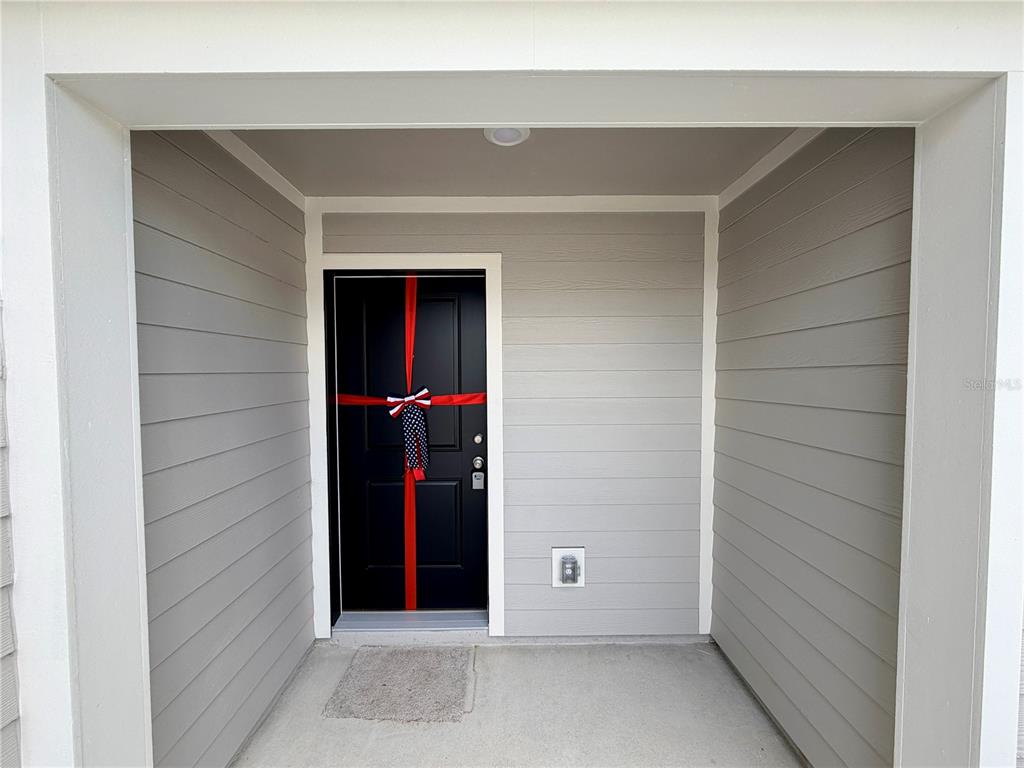 A black front door with a red ribbon sits within a covered gray-sided entryway — 842 LYNX STREET, DAVENPORT, FL