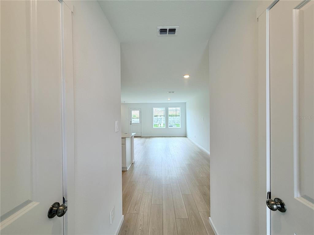 A hallway leads into an open-concept living area with light wood-look flooring and white walls — 842 LYNX STREET, DAVENPORT, FL