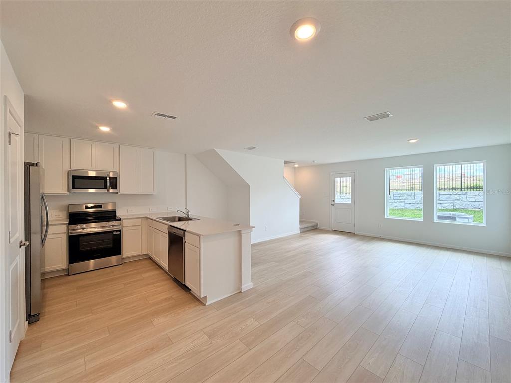 An open-concept kitchen and living area features white cabinetry, stainless steel appliances, and light flooring — 842 LYNX STREET, DAVENPORT, FL