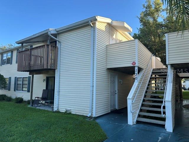 A two-story apartment building features light yellow siding, a wooden balcony, and an exterior staircase — 130 SABAL COURT UNIT H, OLDSMAR, FL