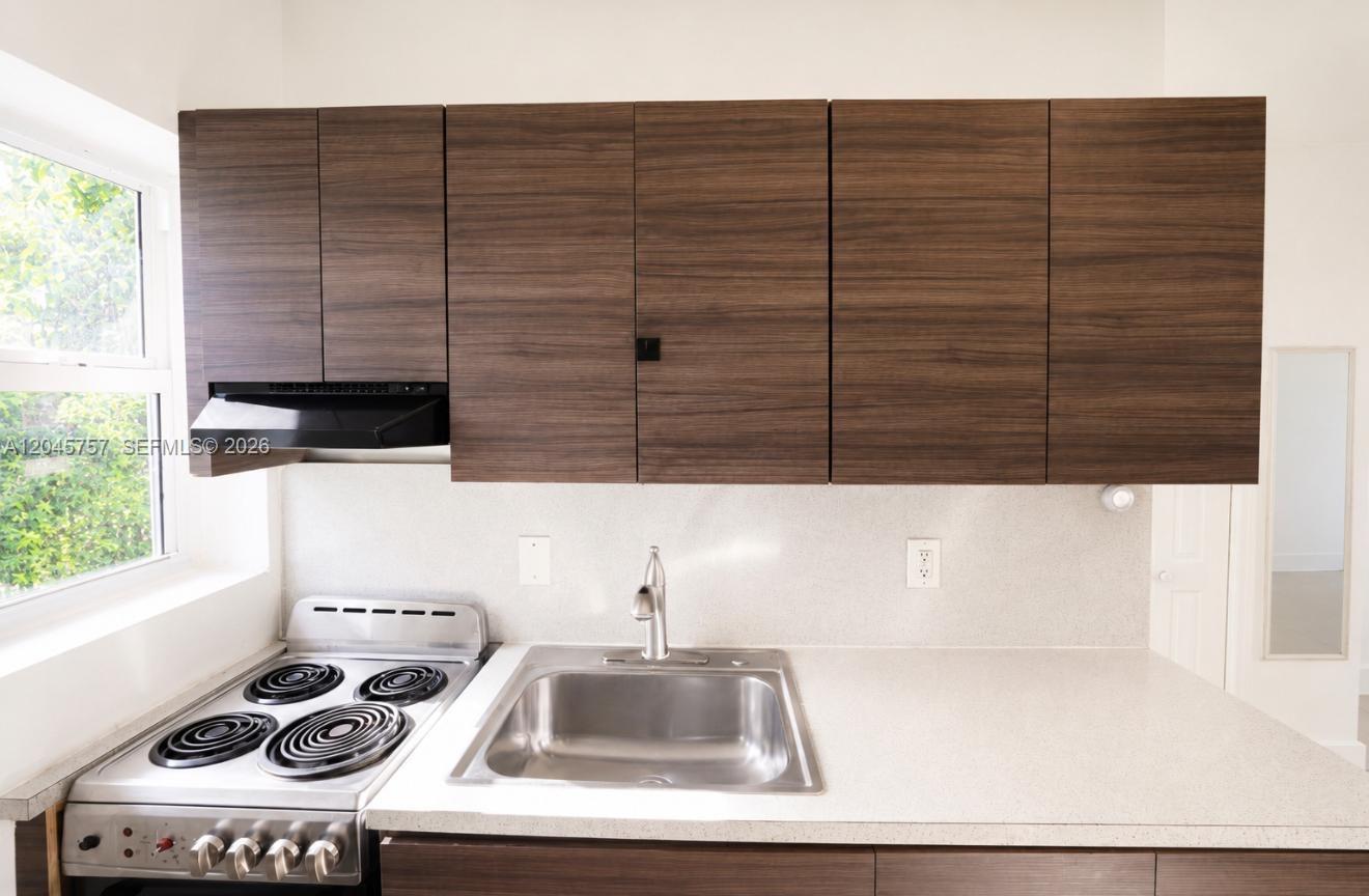 A small kitchen features a stainless steel stove, a sink, and dark wood-grain cabinets — 551 NE 61st St # 4, Miami FL 33137, MIAMI, FL
