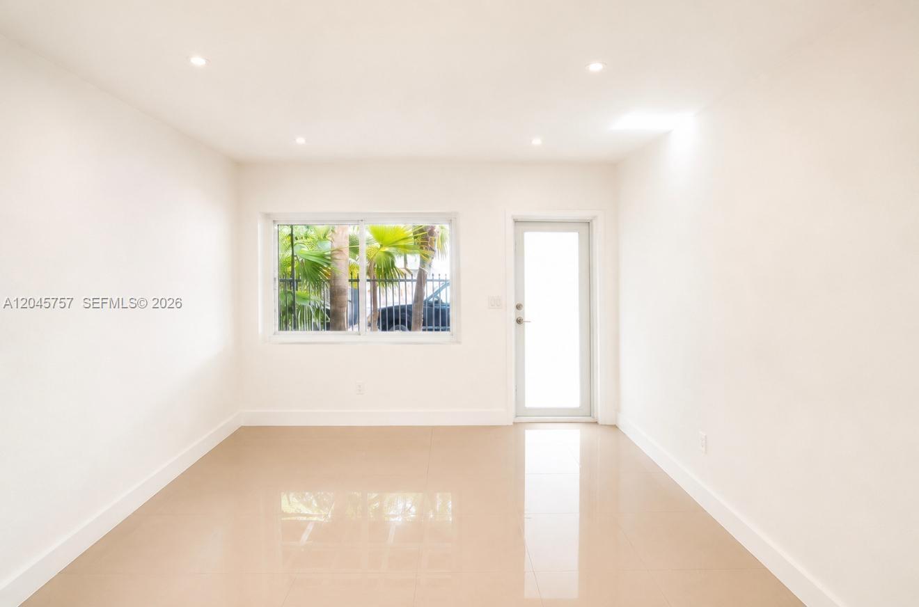 A minimalist room with white walls, beige tile flooring, recessed lighting, a window, and a door — 551 NE 61st St # 4, Miami FL 33137, MIAMI, FL