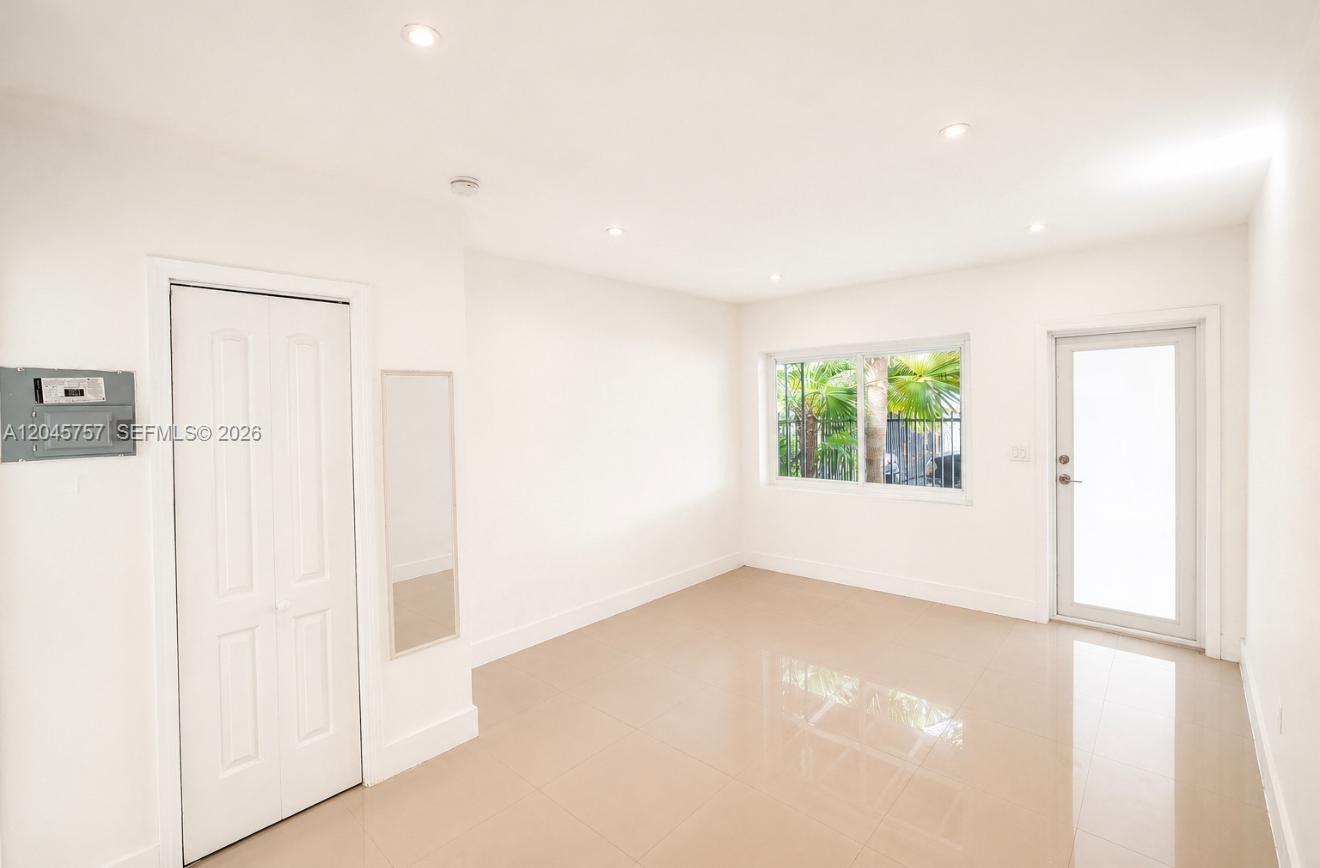 An empty room features white walls, tile flooring, a door, and a window with greenery — 551 NE 61st St # 4, Miami FL 33137, MIAMI, FL