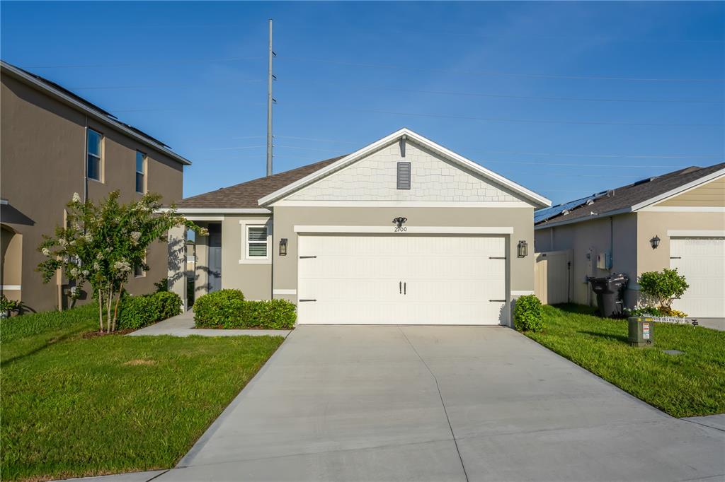 A single-story house with a white garage door, light-colored siding, and a concrete driveway — 2900 WATERLILY WAY, POINCIANA, FL