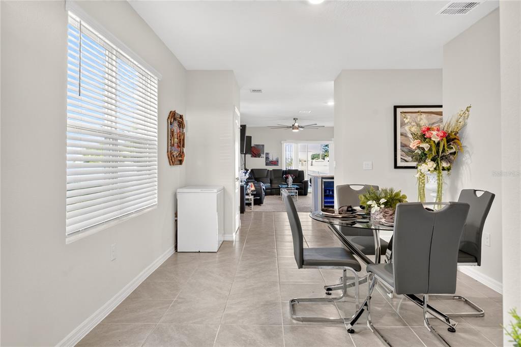 A dining area with tile floors and a glass table leads into a living room — 2900 WATERLILY WAY, POINCIANA, FL