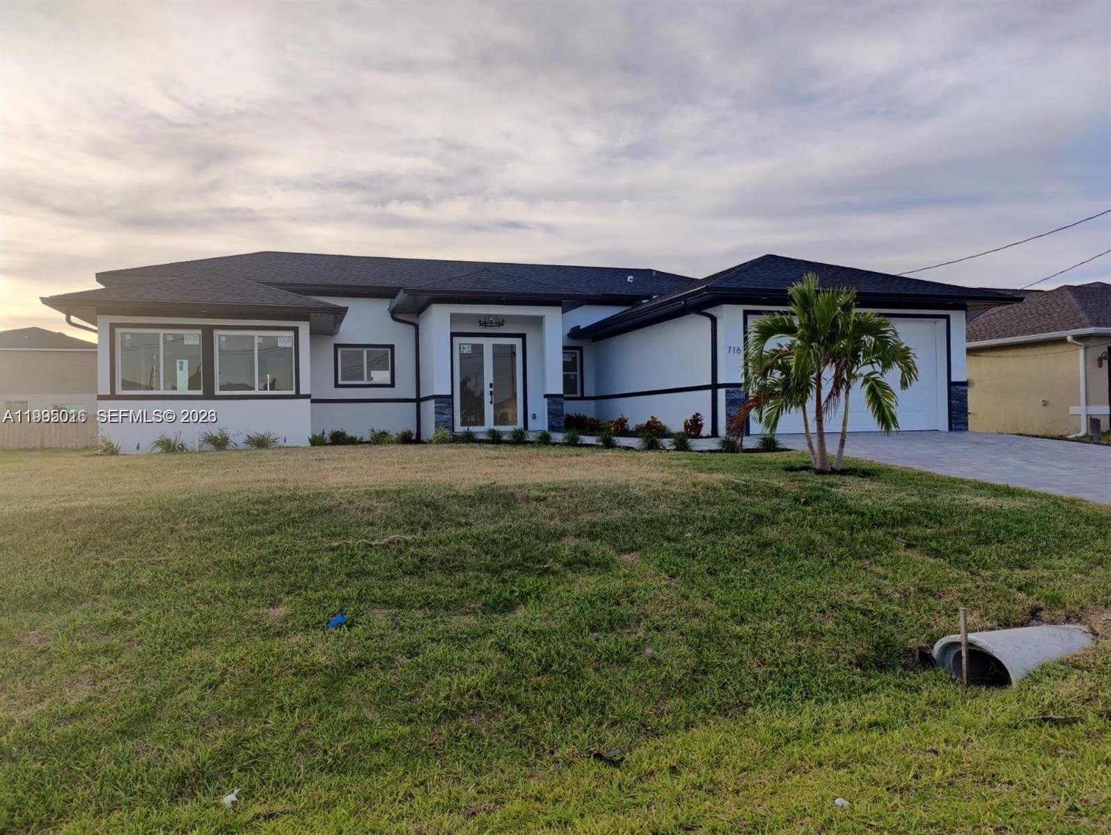A modern, single-story house with white stucco walls, dark trim, and a paved driveway — 716 NW 37TH AVE, Cape Coral FL 33993, CAPE CORAL, FL
