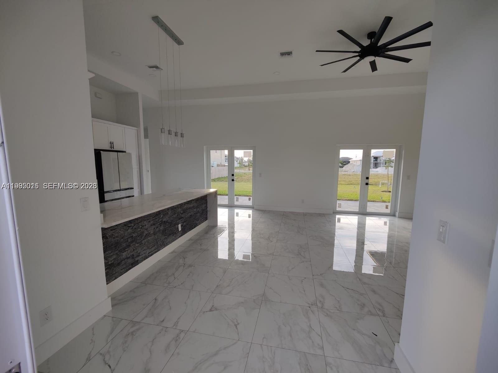 A modern kitchen and living area feature white marble floors, a stone-faced island, and glass doors — 716 NW 37TH AVE, Cape Coral FL 33993, CAPE CORAL, FL