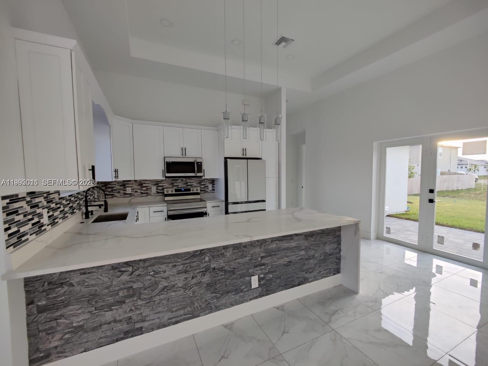 A modern kitchen features white cabinetry, a stone-accented island, and marble-look tile flooring — 716 NW 37TH AVE, Cape Coral FL 33993, CAPE CORAL, FL