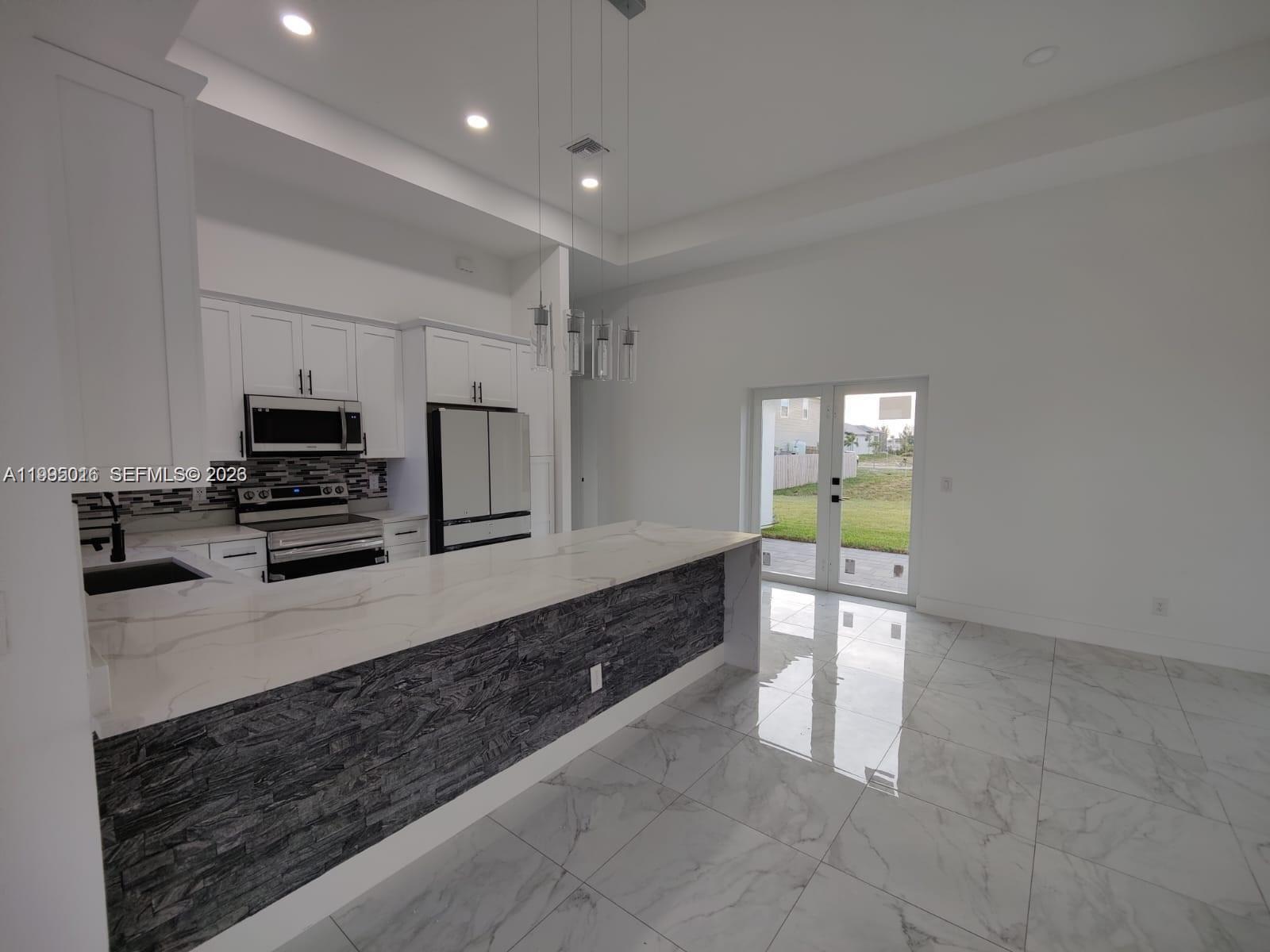 A modern kitchen features white cabinets, a stone-accented island, and marble-look tile flooring — 716 NW 37TH AVE, Cape Coral FL 33993, CAPE CORAL, FL