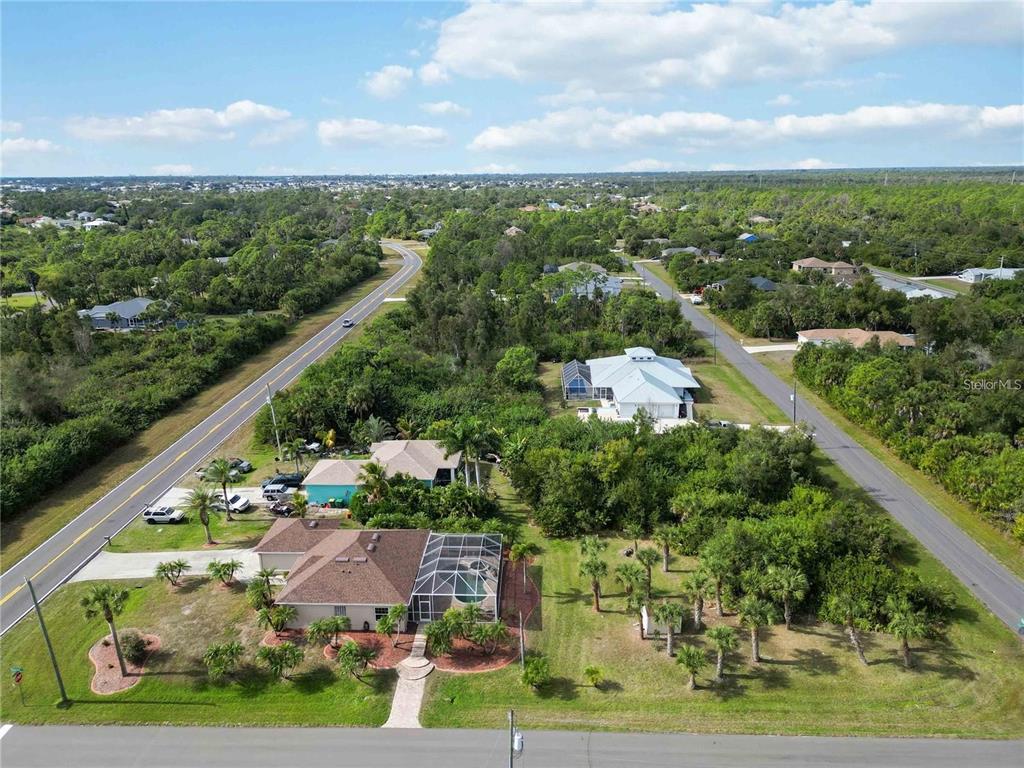 An aerial view shows two houses with screened-in pools surrounded by trees and paved roads — 9424 WILLMINGTON BOULEVARD, ENGLEWOOD, FL