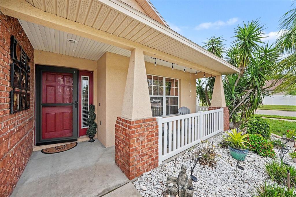A covered front porch with a red door, brick accents, and white railings — 12337 ROSE HAVEN BOULEVARD, NEW PORT RICHEY, FL