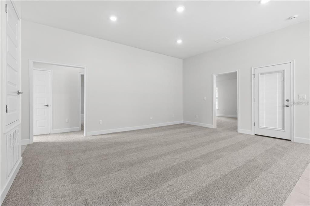 A spacious, carpeted room with white walls, recessed lighting, and three interior doors — 87 RAMBLEWOOD DRIVE, PALM COAST, FL