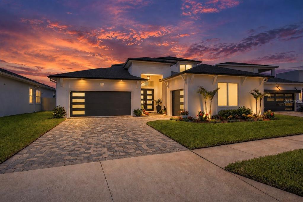 A modern white house with a paved driveway and a dark garage at sunset — 10706 TORCHWOOD SEA WAY, SAN ANTONIO, FL