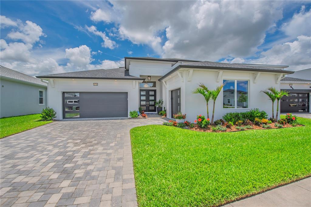 A modern white single-story house features a gray garage door and a paved driveway — 10706 TORCHWOOD SEA WAY, SAN ANTONIO, FL
