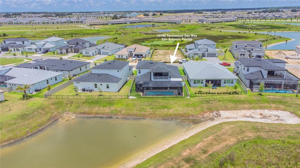An aerial view shows a suburban neighborhood with houses, a swimming pool, and a pond — 10706 TORCHWOOD SEA WAY, SAN ANTONIO, FL