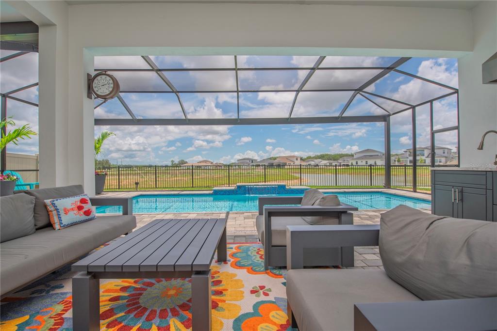 A covered patio features outdoor furniture, a colorful rug, and a screened-in swimming pool — 10706 TORCHWOOD SEA WAY, SAN ANTONIO, FL