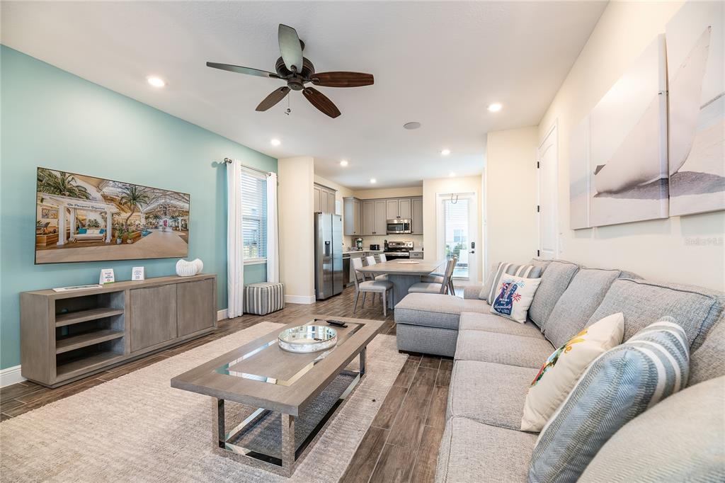 An open-concept living room features a blue accent wall, gray sectional sofa, and kitchen — 8031 KNEE DEEP ROAD, KISSIMMEE, FL