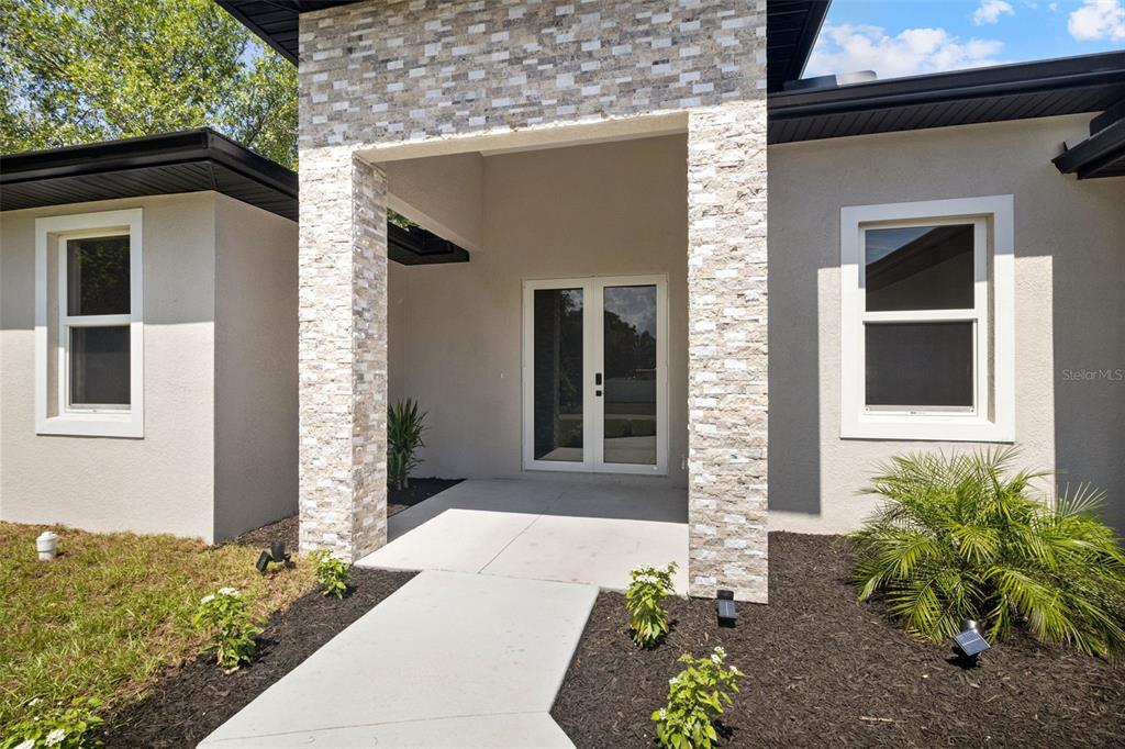 The exterior of a house features a stone-accented entryway with double glass doors — 1099 CAZENOVIA STREET, PORT CHARLOTTE, FL