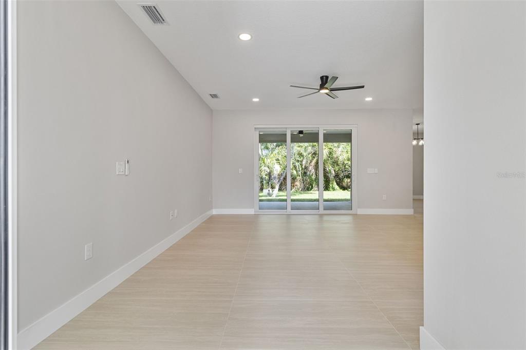 A bright, empty living room features light-colored tile flooring, a ceiling fan, and sliding glass doors — 1099 CAZENOVIA STREET, PORT CHARLOTTE, FL