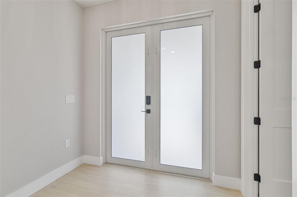 A room with light-colored walls, wood-look flooring, and a set of frosted glass double doors — 1099 CAZENOVIA STREET, PORT CHARLOTTE, FL