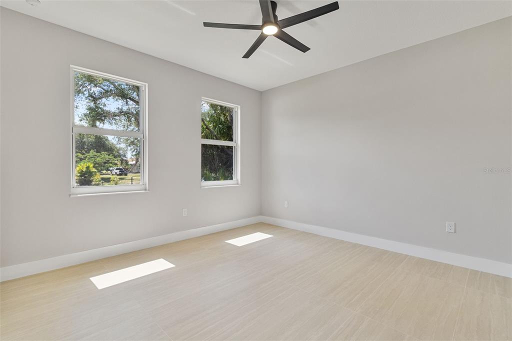 A bright bedroom features light-colored tile flooring, two windows, and a ceiling fan — 1099 CAZENOVIA STREET, PORT CHARLOTTE, FL
