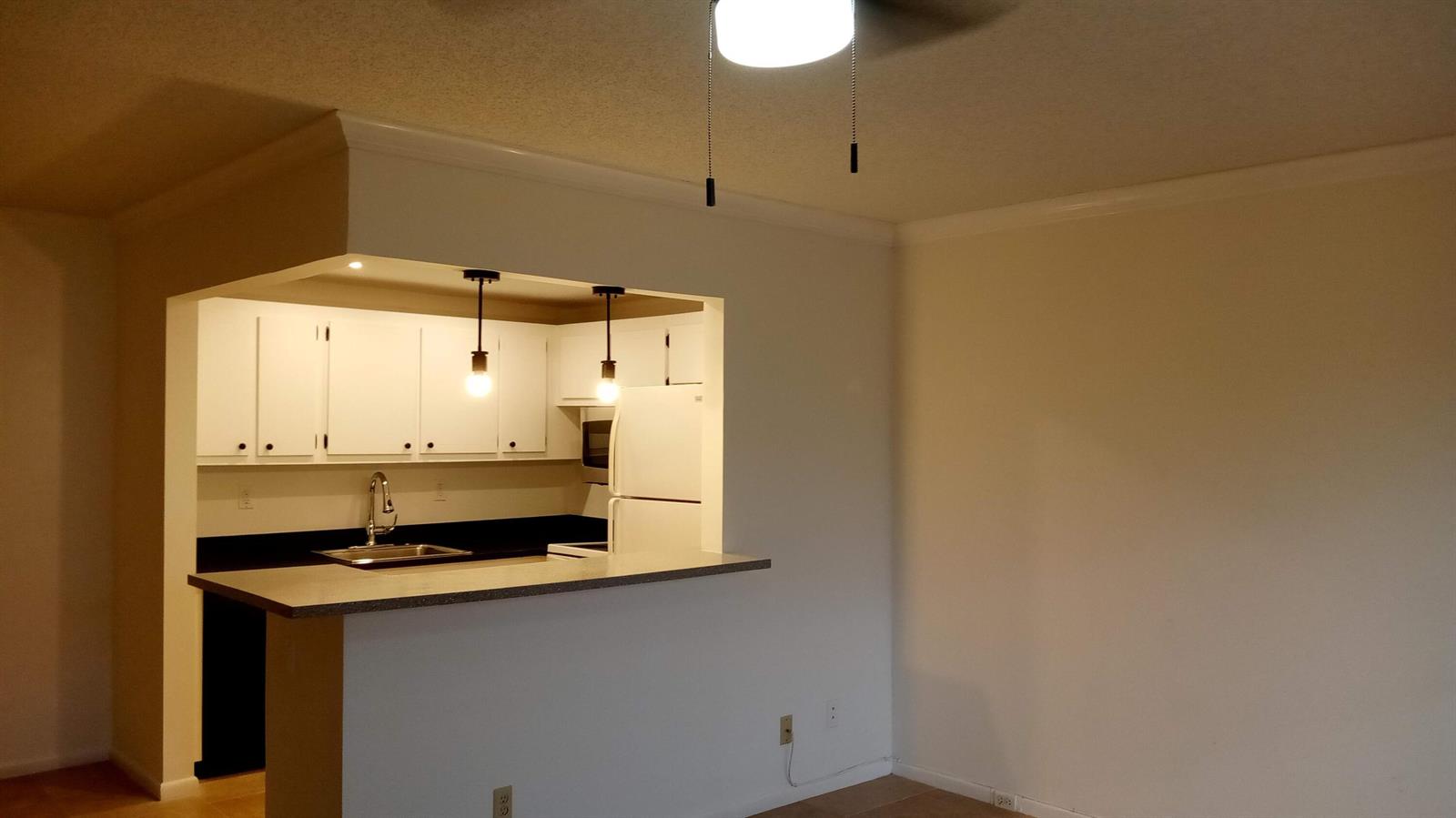 A kitchen with white cabinets and a breakfast bar opens into a living area — 16 Dorset A, Boca Raton FL 33434, BOCA RATON, FL