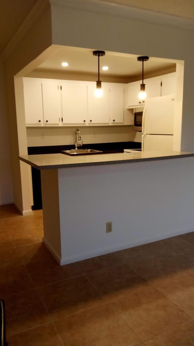 A kitchen with white cabinets, dark countertops, and a breakfast bar overlooking a tiled floor — 16 Dorset A, Boca Raton FL 33434, BOCA RATON, FL