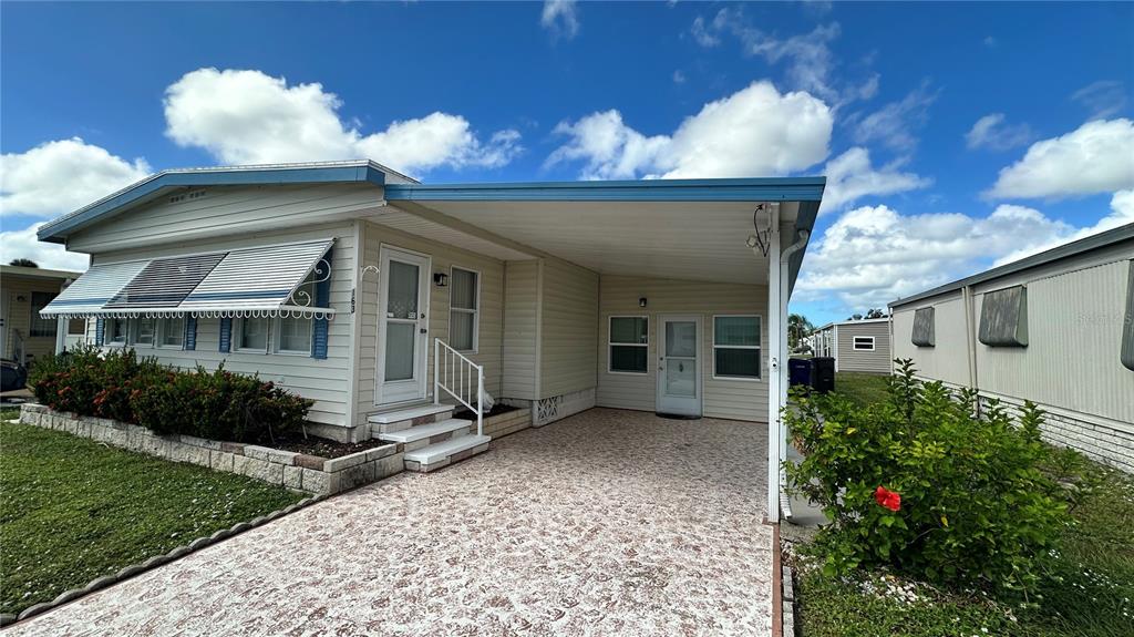 A single-story manufactured home with a carport, light siding, and a patterned concrete driveway — 5619 BAYSHORE ROAD UNIT 163, PALMETTO, FL