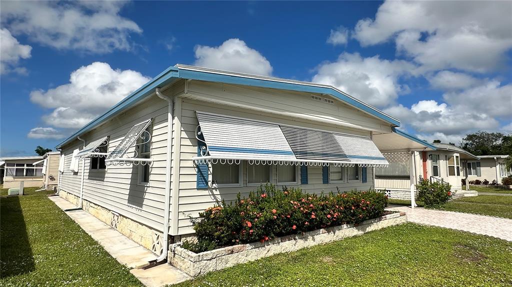 A light-colored mobile home features horizontal siding, metal window awnings, and a landscaped garden bed — 5619 BAYSHORE ROAD UNIT 163, PALMETTO, FL