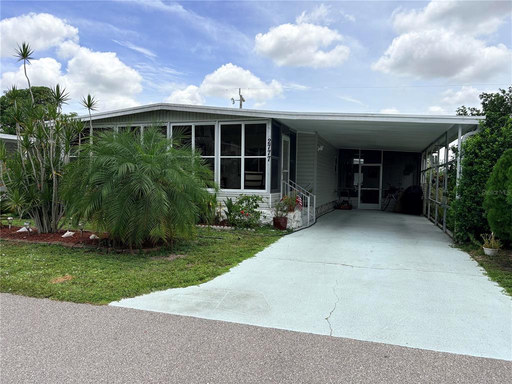 A single-story manufactured home features a light gray exterior, a carport, and a front porch — 2777 INDIANWOOD DRIVE, NORTH FORT MYERS, FL