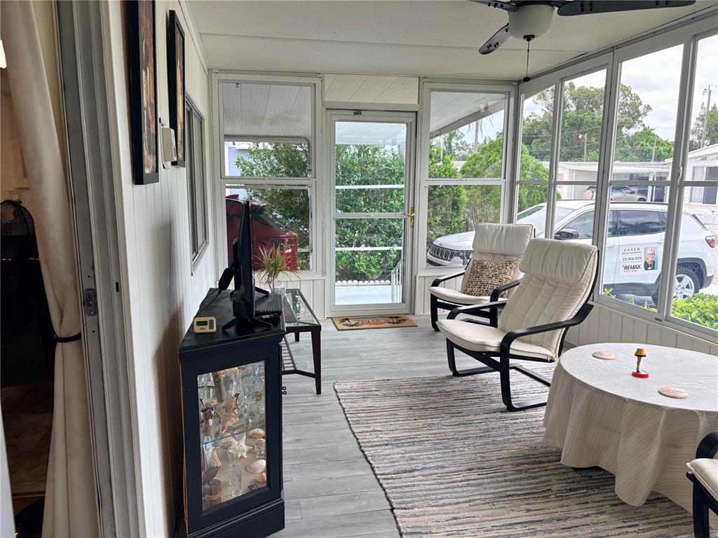 A sunroom features light wood-look flooring, two white armchairs, a display cabinet, and large windows — 2777 INDIANWOOD DRIVE, NORTH FORT MYERS, FL