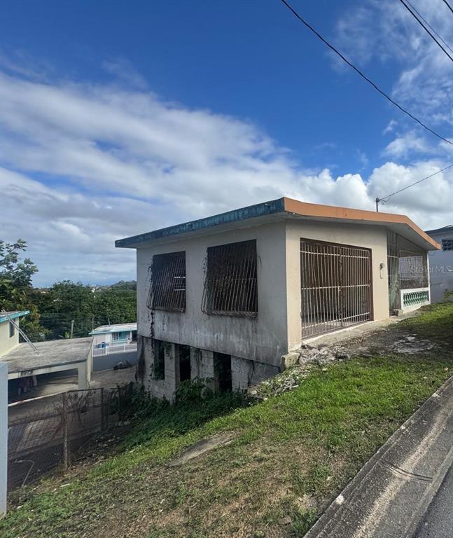 A two-story concrete house with barred windows and a garage sits on a grassy slope — 487 EXT. VILLA DEL RIO, TOA ALTA, PR