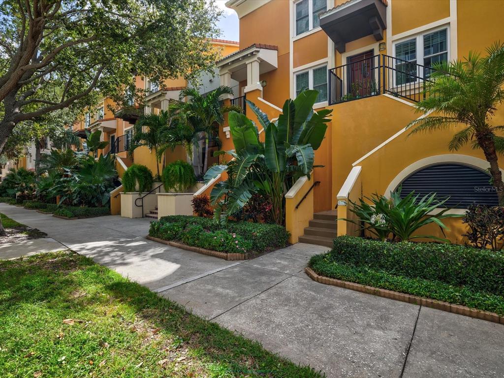 A row of yellow townhouses with stairs leading to elevated front entrances and lush landscaping — 100 4TH AVENUE S UNIT 416, ST PETERSBURG, FL