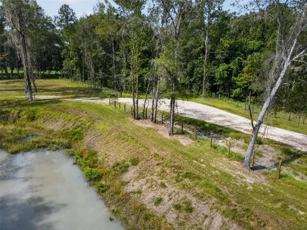 An aerial view shows a dirt driveway running alongside a pond and a wooded area — NW 128TH TERRACE Lot 36, REDDICK, FL