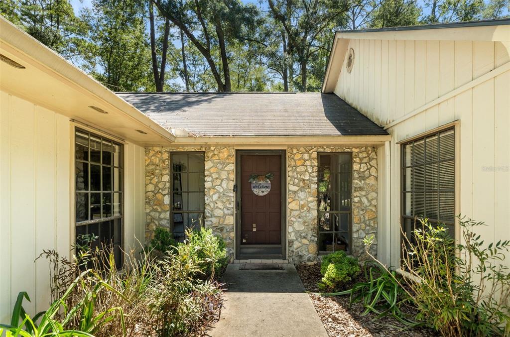 The exterior of a house features a stone facade, a brown front door, and large windows — 1317 SW 98TH STREET, GAINESVILLE, FL