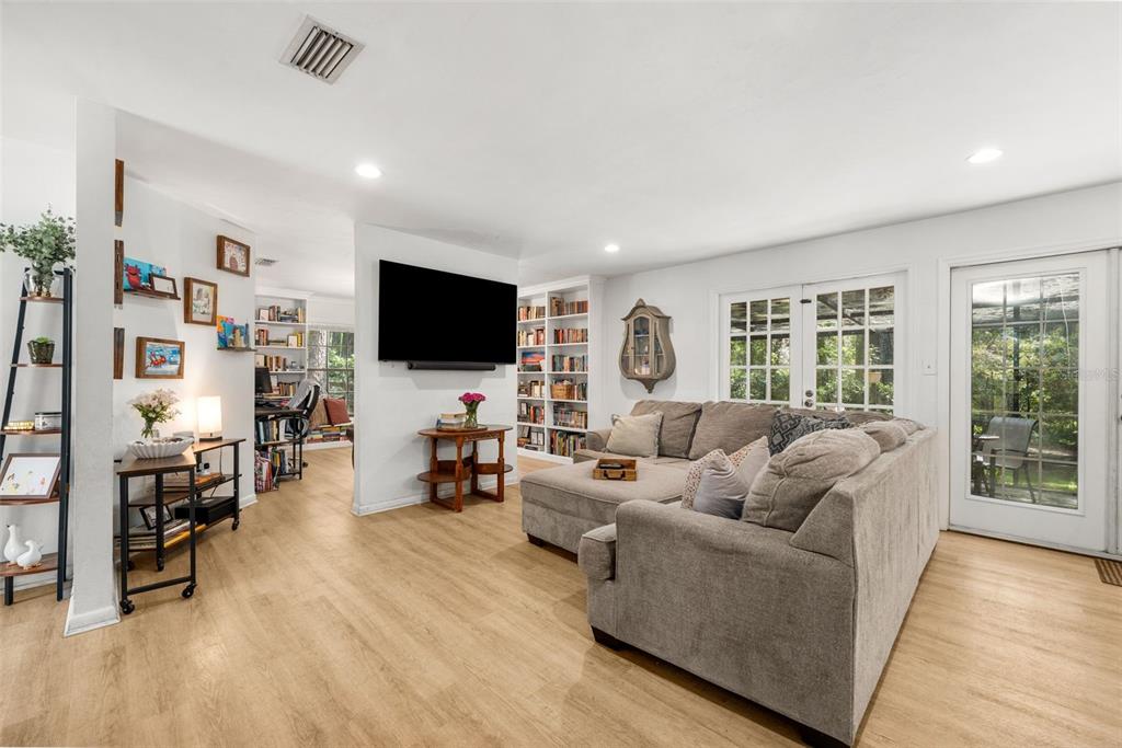A living room with light wood floors, a sectional sofa, a wall-mounted TV, and bookshelves — 1317 SW 98TH STREET, GAINESVILLE, FL