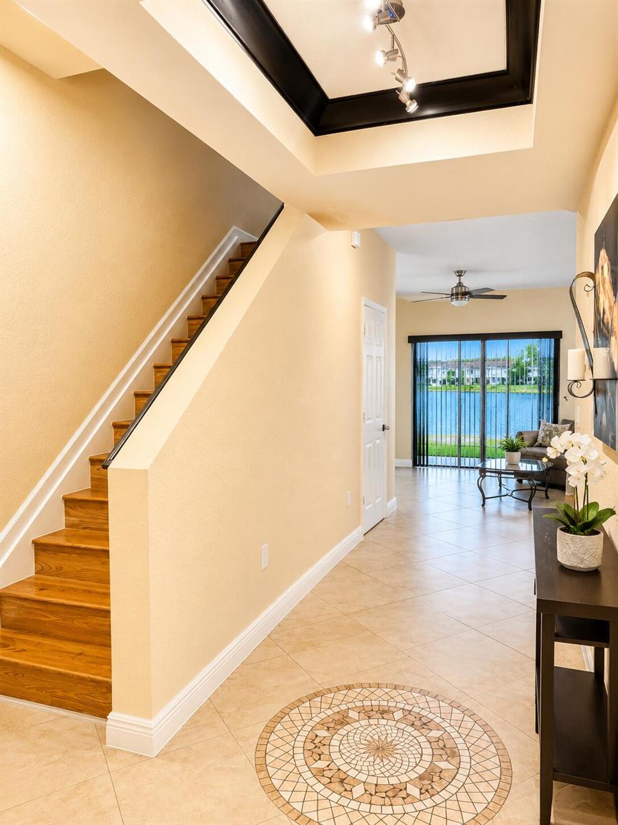 A foyer with a wooden staircase, tile flooring, and a view of a lake outside — 4206 Emerald Vista, Lake Worth FL 33461, LAKE WORTH, FL