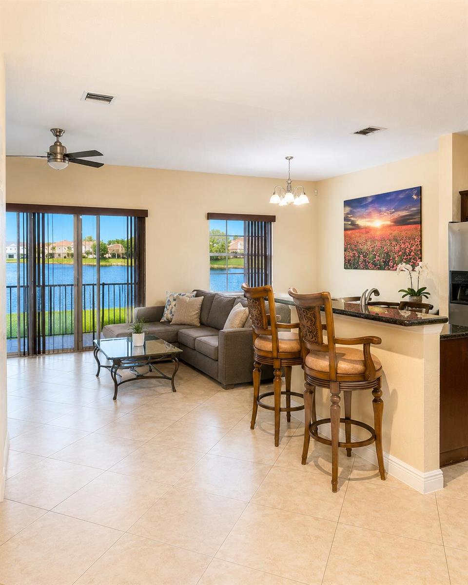 A living room with tile floors, a grey sectional, and a breakfast bar facing a lake — 4206 Emerald Vista, Lake Worth FL 33461, LAKE WORTH, FL
