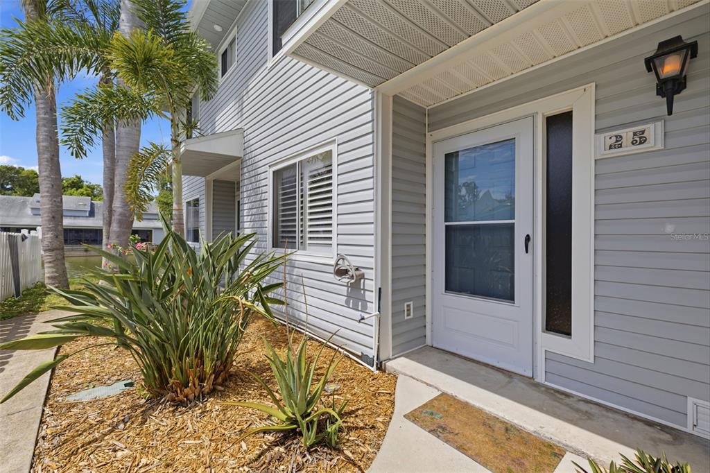 The exterior of a gray-sided house features a front door, a window, and landscaping — 500 NEW YORK AVENUE UNIT 25, DUNEDIN, FL