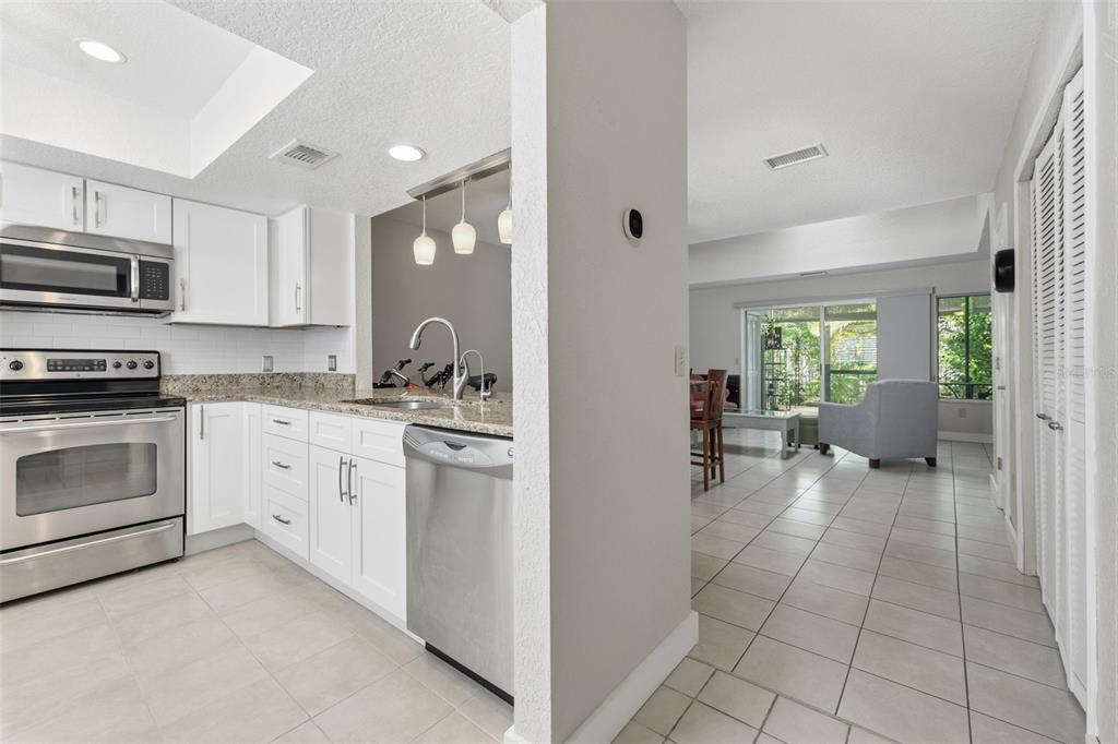 A kitchen with white cabinets and stainless steel appliances opens into a tiled living area — 500 NEW YORK AVENUE UNIT 25, DUNEDIN, FL