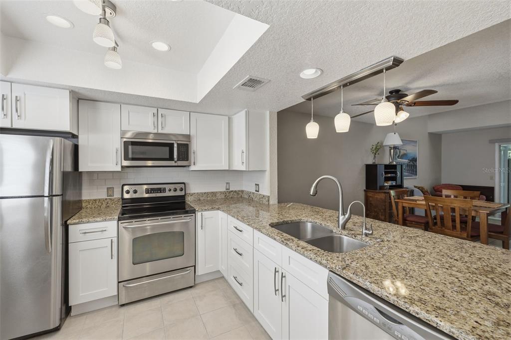 A kitchen with white cabinets, granite countertops, stainless steel appliances, and a breakfast bar — 500 NEW YORK AVENUE UNIT 25, DUNEDIN, FL