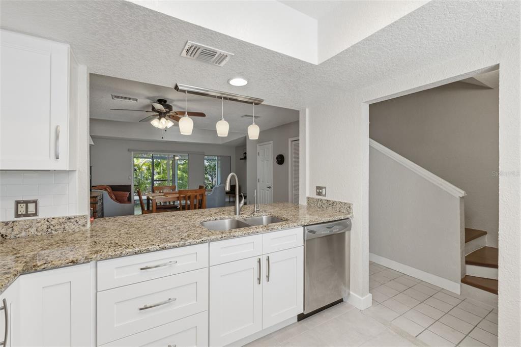 A kitchen with white cabinets, granite countertops, and a stainless steel dishwasher overlooks a dining area — 500 NEW YORK AVENUE UNIT 25, DUNEDIN, FL