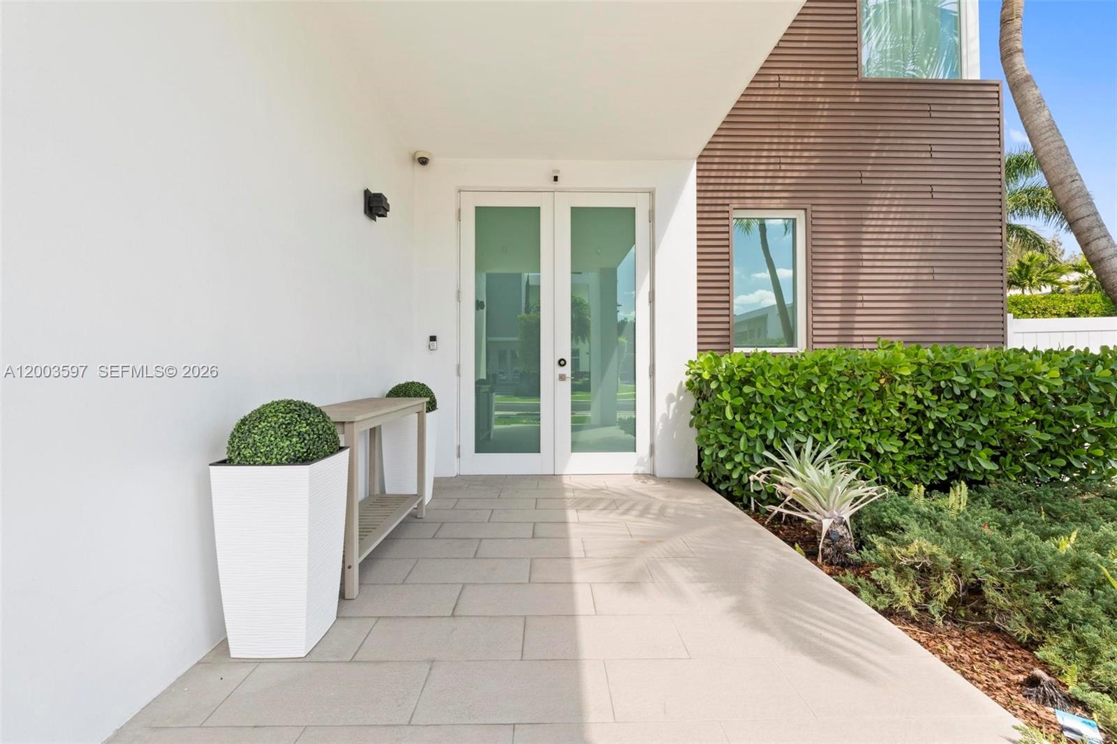 A modern entryway features double glass doors, a tiled porch, and a wooden accent wall — 10431 NW 68th Ter, Doral FL 33178, DORAL, FL