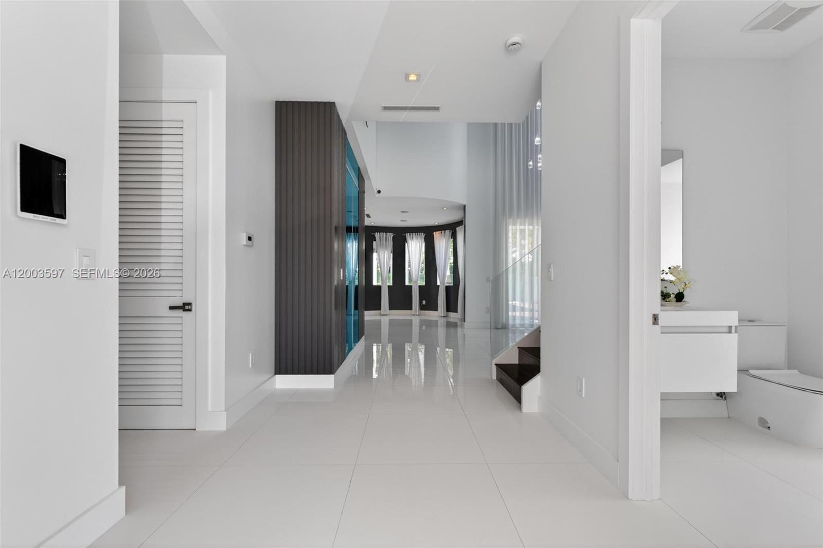 A bright hallway with white tile floors leads toward a curved wall with windows — 10431 NW 68th Ter, Doral FL 33178, DORAL, FL