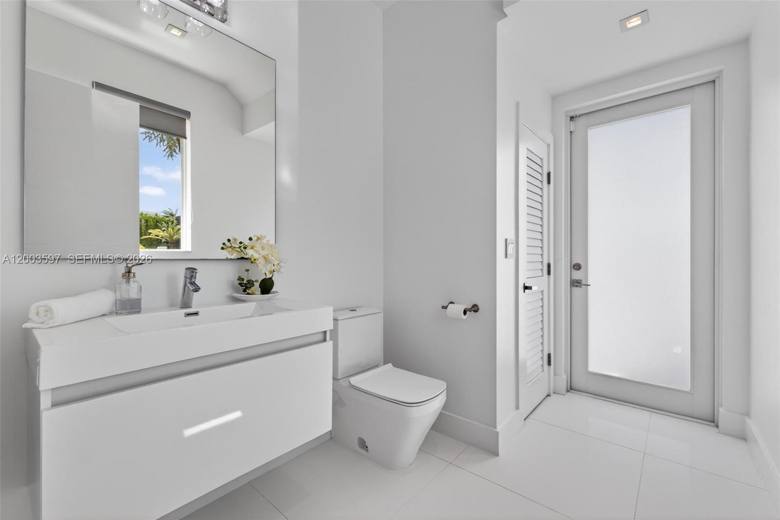 A modern white bathroom features a floating vanity, a toilet, and a frosted glass door — 10431 NW 68th Ter, Doral FL 33178, DORAL, FL