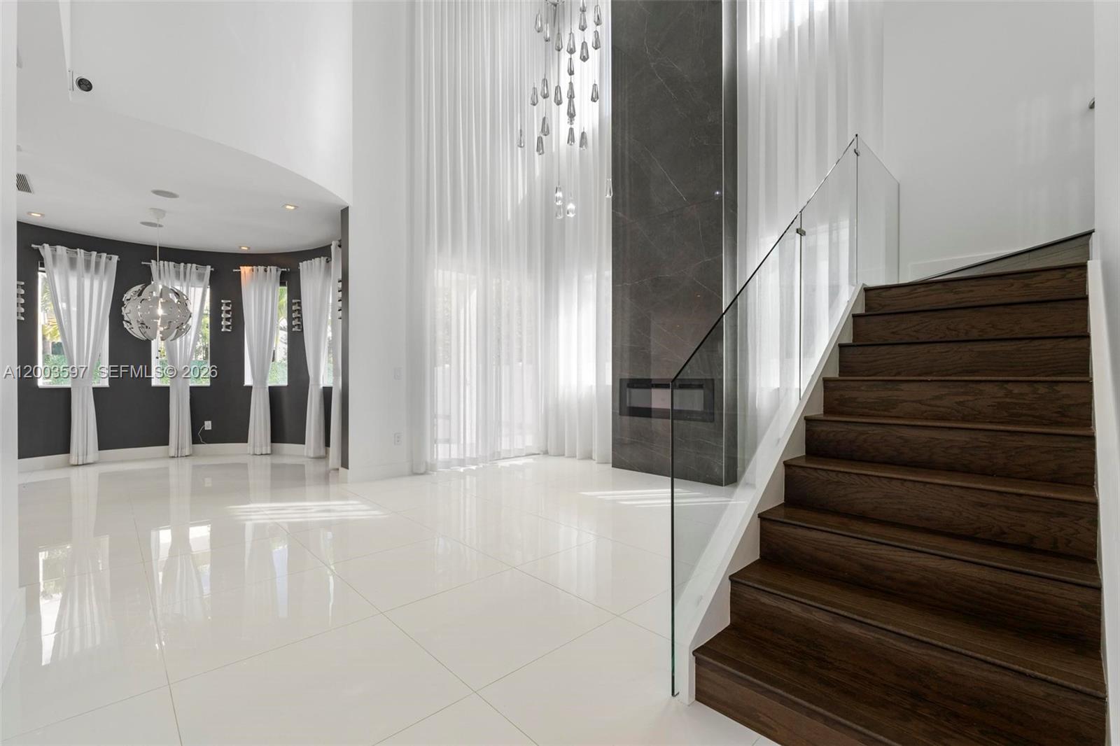 A modern living room features a double-height ceiling, dark wood staircase, and a stone fireplace — 10431 NW 68th Ter, Doral FL 33178, DORAL, FL