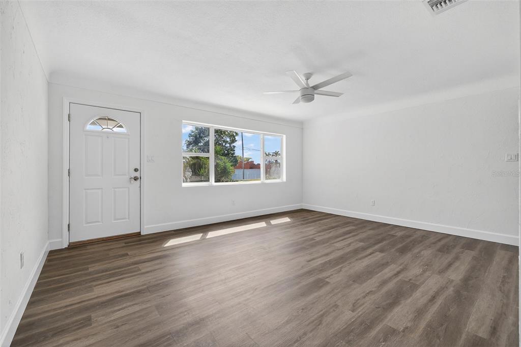 An empty living room with white walls, wood-look flooring, a ceiling fan, and a front door — 211 89TH AVENUE N, ST PETERSBURG, FL